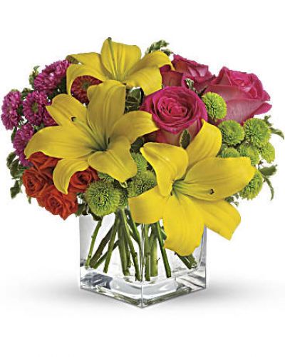 Splash into spring! Sun-bright yellow, hot pink and orange blooms add up to a sensational and oh-so-stylish spring & summer floral arrangement for any occasion.
Hot pink and orange roses are mixed with yellow asiatic lilies, hot pink matsumoto asters and lime green button spray chrysanthemums in a clear glass cube vase.